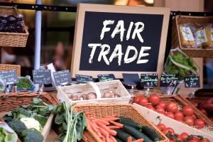Ein Schild mit der Aufschrift "Fair Trade" davor verschiedene Gemüsesorten und Preisschilder