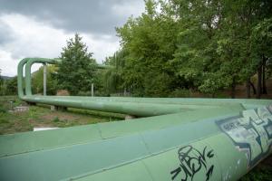 grüne angestrichene Fermwärmeleitungen durchziehen oberirdisch die Landschaft vor Jena