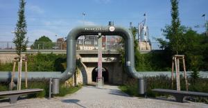 Eine Fernwärmeleitung verläuft ebenerdig und über den Eingang einer Unterführung über einen Bahnschiene. Im Hintergund ist der Jentower zu sehen. f