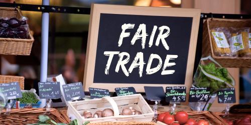 Ein Schild mit der Aufschrift "Fair Trade" davor verschiedene Gemüsesorten und Preisschilder